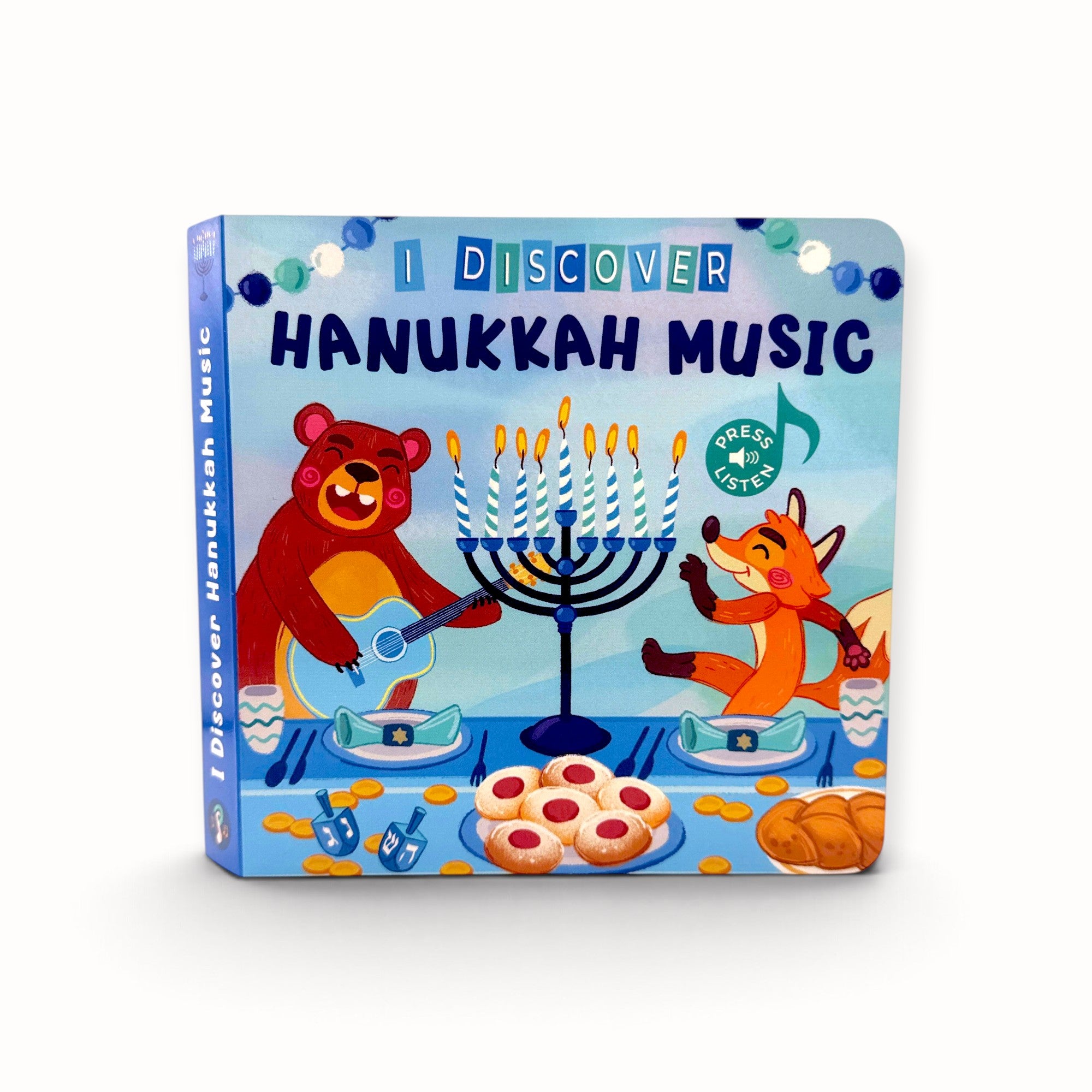 A children's board book titled 'I Discover Hanukkah Music' featuring colorful cartoon illustrations of a bear and a fox playing around a menorah on a light blue background.