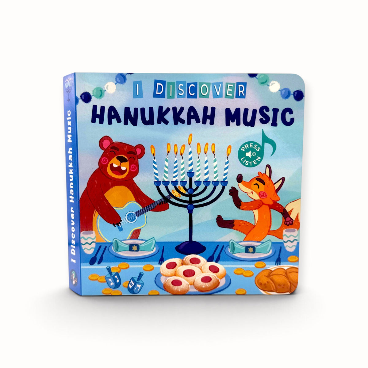 A children's board book titled 'I Discover Hanukkah Music' featuring colorful cartoon illustrations of a bear and a fox playing around a menorah on a light blue background.